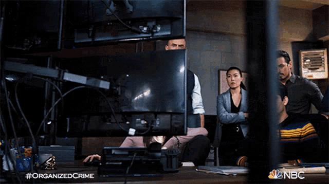 a group of people looking at a computer screen with a nbc logo in the corner