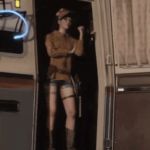 a woman standing in a doorway holding a gun and wearing a hat that says ' texas ' on it