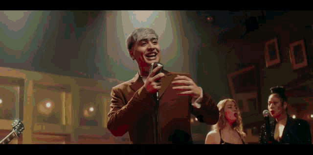 a man in a suit is singing into a microphone in front of a group of people .