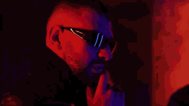 a man with a beard and sunglasses is smoking a cigarette in a dark room .