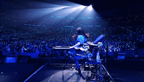 a woman in a blue dress is playing a keyboard on stage in front of a crowd that is glowing in blue
