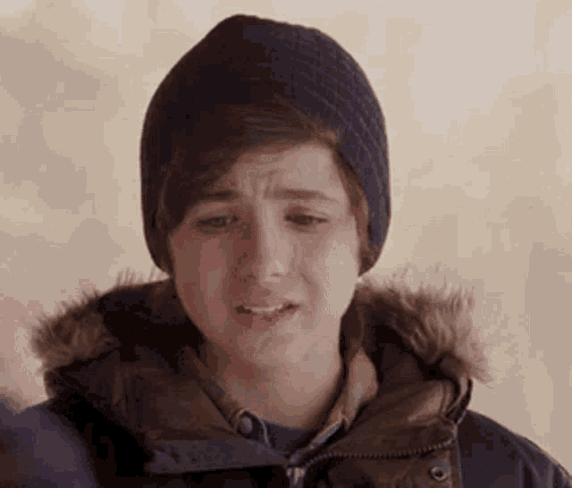 a young boy wearing a hat and jacket is crying .