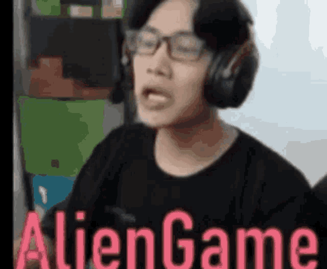 a man wearing headphones and glasses is making a funny face and the words aliengame are above him .