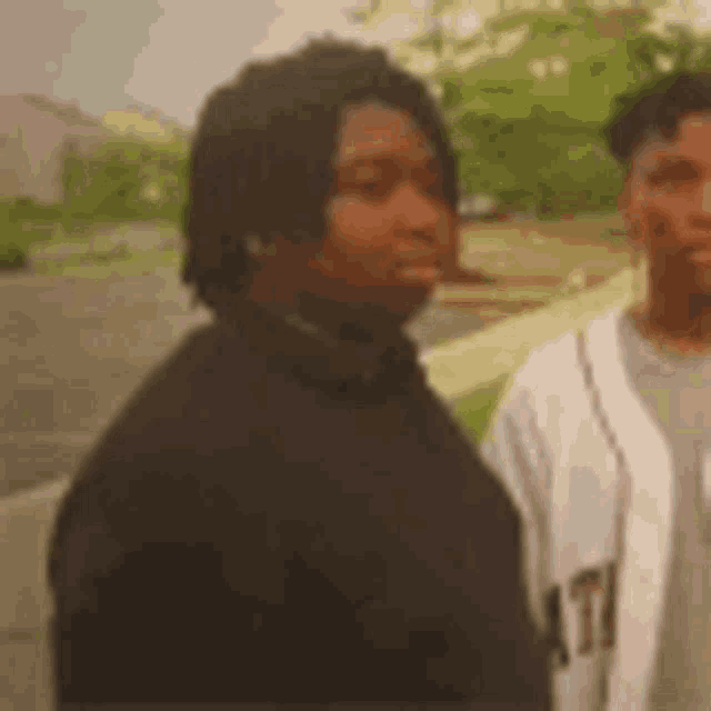 two men are standing next to each other on a sidewalk in a park .