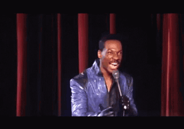 a man singing into a microphone in front of a red curtain