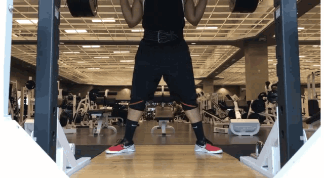 a man squatting down in a gym with a nike shoe on