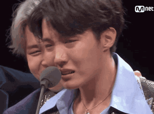 a man is crying in front of a microphone while another man laughs behind him