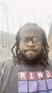 a man with dreadlocks wearing glasses and a shirt that says mind