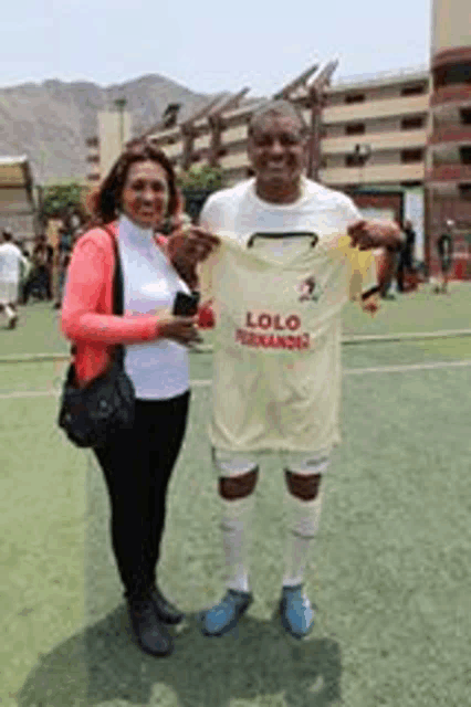a man and a woman are standing next to each other on a soccer field holding a soccer jersey .