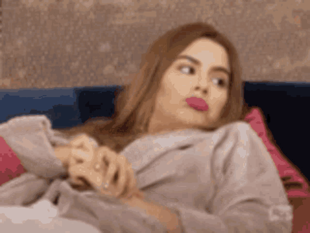 a woman is laying on a couch with her hands folded and making a face .