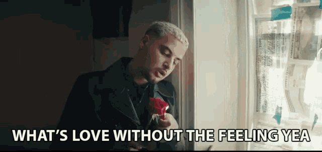 a man is holding a red rose in front of a window with the words what 's love without the feeling yea below him