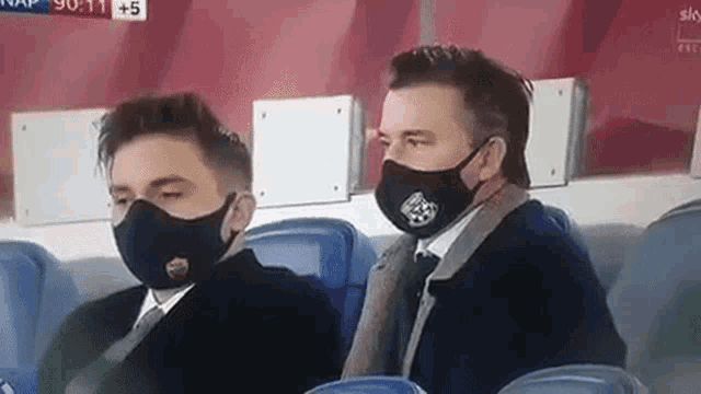 two men wearing masks are sitting in a stadium .