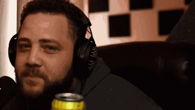 a man with a beard wearing headphones is sitting in front of a microphone holding a can of soda .