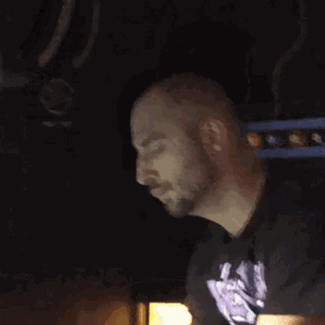 a man with a beard is wearing a black shirt with a purple logo on the front