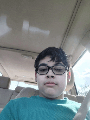 a young boy wearing glasses and a green shirt is sitting in the back seat of a car