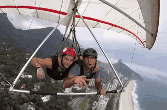 a man in a red helmet is flying a hang glider over a city
