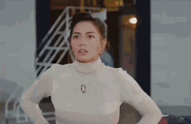 a woman in a white turtleneck sweater and necklace is standing in front of a building .