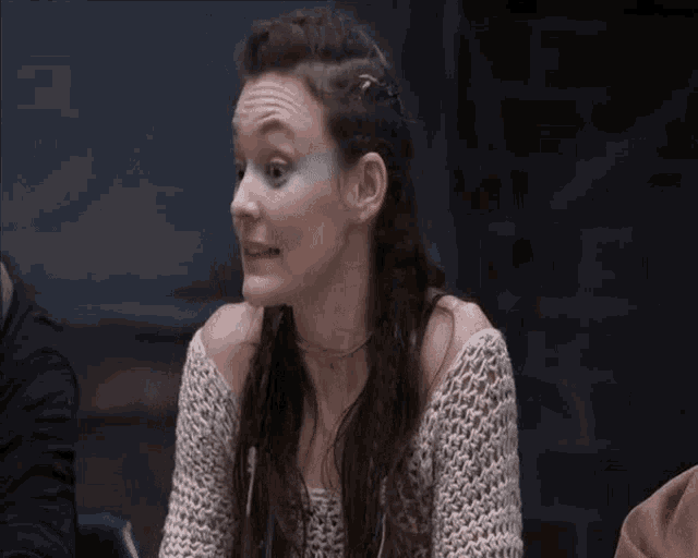 a woman in a white sweater is sitting at a table making a funny face .