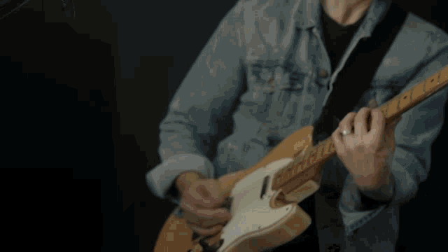 a man in a denim jacket plays a guitar