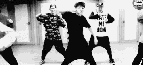 a black and white photo of a group of young men dancing in a room .