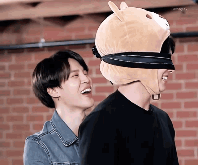 two men are laughing and one has a stuffed animal on his head