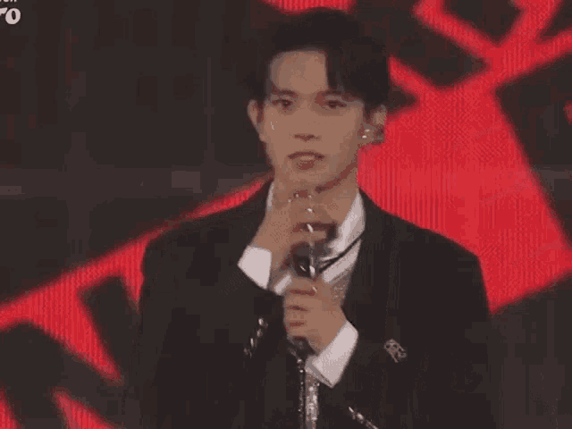 a young man in a suit is standing on a stage holding his hand to his chest .