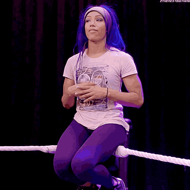 a woman with blue hair is sitting on a rope in a wrestling ring ..