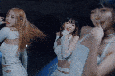 a group of women are dancing in a dark room and one of them is wearing a white top
