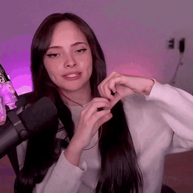 a woman with long dark hair is sitting in front of a microphone and making a heart shape with her hands .