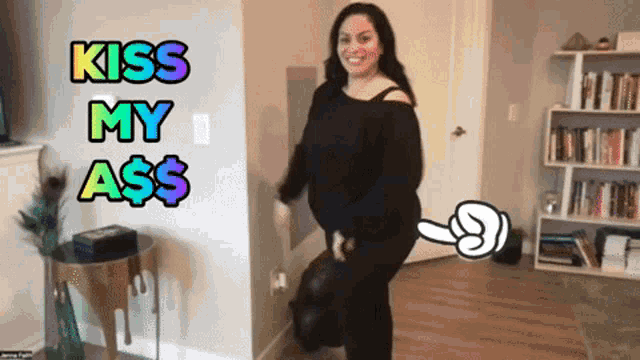 a woman standing in a living room with the words kiss my ass written above her