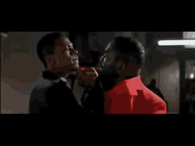 two men are standing next to each other and one is wearing a red jacket
