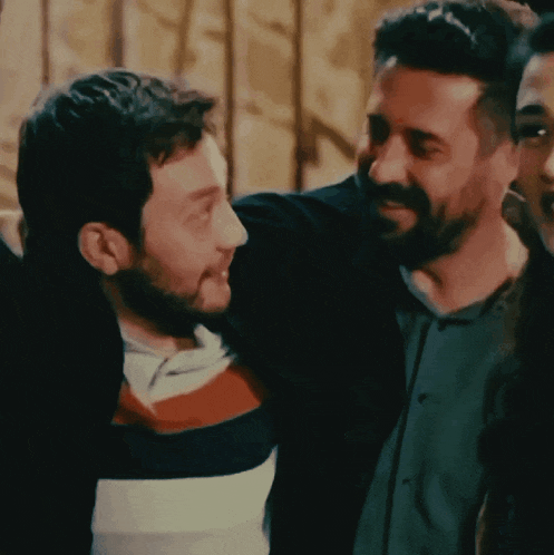 a man with a beard is hugging another man with a striped shirt