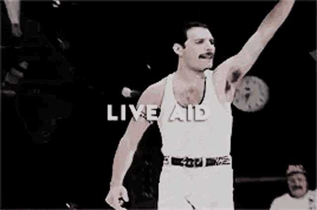 a man in a white tank top is standing on a stage with his arms outstretched .