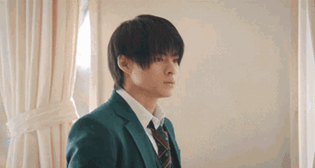 a young man wearing a suit and tie is looking out a window