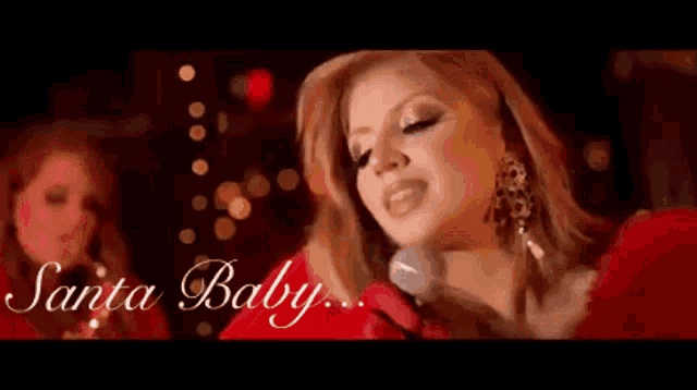 a woman in a red dress singing into a microphone with the words santa baby behind her