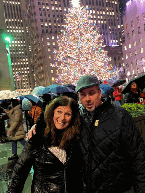 a man and a woman are posing in front of a christmas tree