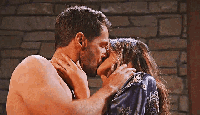 a man and woman kissing in front of a brick wall .