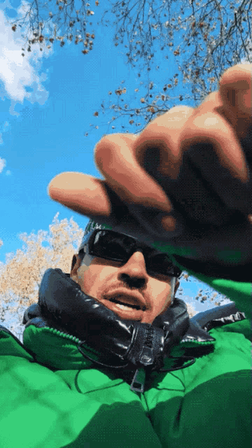 a man wearing sunglasses and a green jacket is taking a picture
