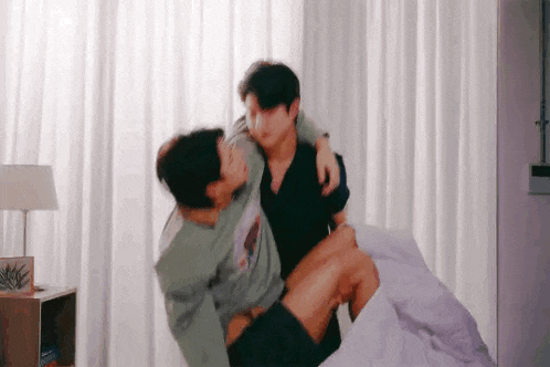 a man is carrying another man on his shoulders while they are sitting on a bed .