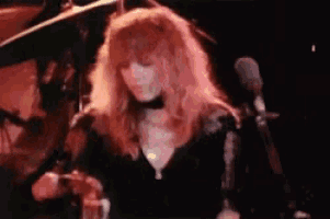 a woman with long red hair is singing into a microphone on stage .