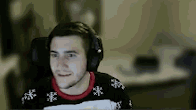 a man wearing headphones and a sweater is sitting in front of a computer .