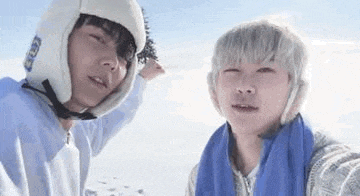 two young men wearing hats and scarves are standing next to each other on a snowy hill .