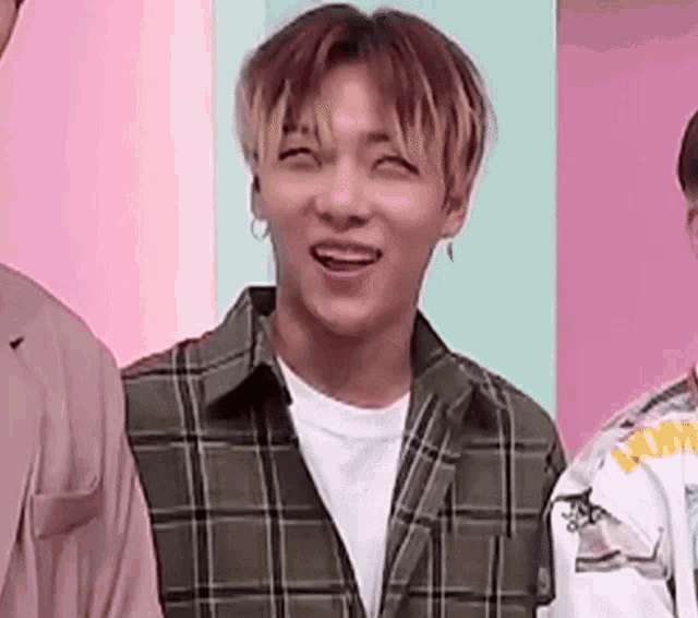 a young man wearing a plaid shirt and earrings is smiling .