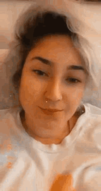 a close up of a woman 's face with a nose ring and a white t-shirt .