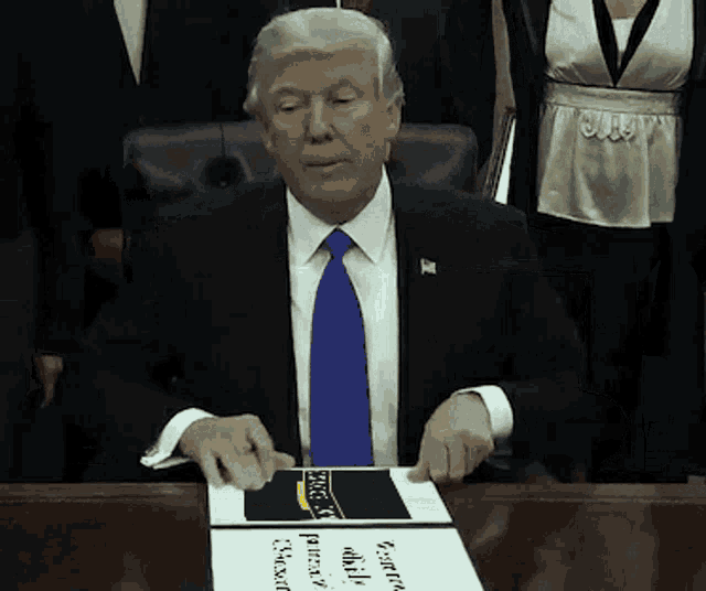 a man in a suit and tie is sitting at a table with a sign that says " george x. "