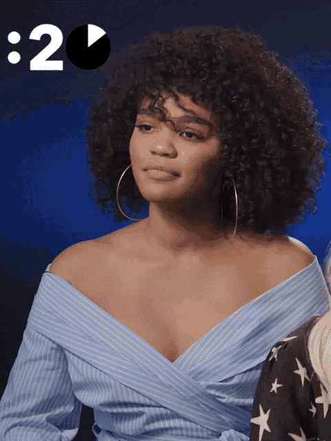 a woman with curly hair wearing hoop earrings and a blue off the shoulder shirt