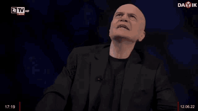 a bald man in a black suit is giving a speech on a tv show