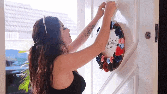 a woman hanging a wreath on a door that says welcome