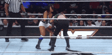 a woman in a wrestling ring with a referee and a wwe logo in the background
