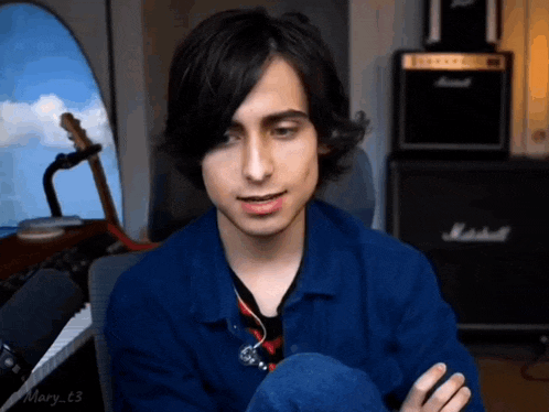 a young man in a blue jacket is sitting in front of a microphone in a room .